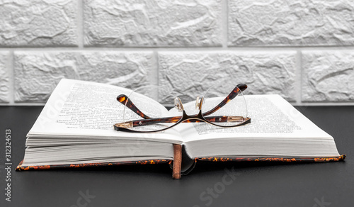 Opened book with eyeglasses on black table.