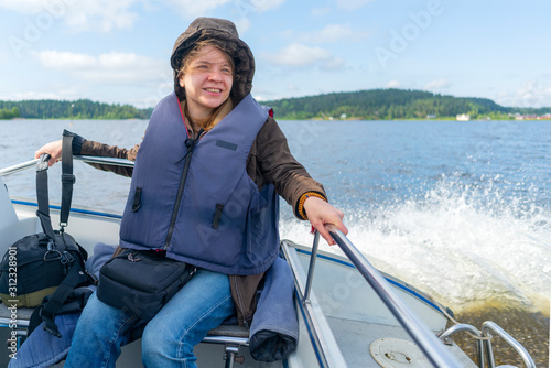 Girl in life jacket on boat. Splashing waves.