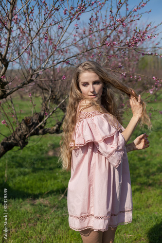 Beautiful blonde woman in pink dress in flowering garden in spring