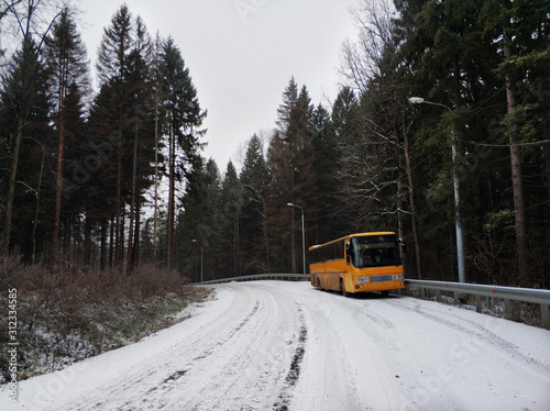 An old orange bus is abandoned on a snowy road in the woods. Winter landscape with frosty road, forest and forgotten vintage bus