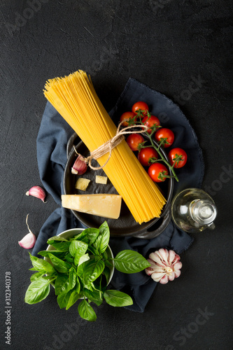 Raw ingredients for cooking spaghetti on a black background. Pasta, tomatoes, garlic, basel and parmesan