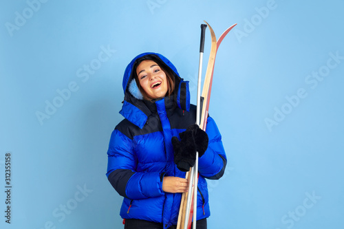 Skii lover. Caucasian woman's portrait on blue studio background. Beautiful female model in warm clothes. Concept of human emotions, facial expression, sales, ad. Winter mood, Christmas time, holidays photo