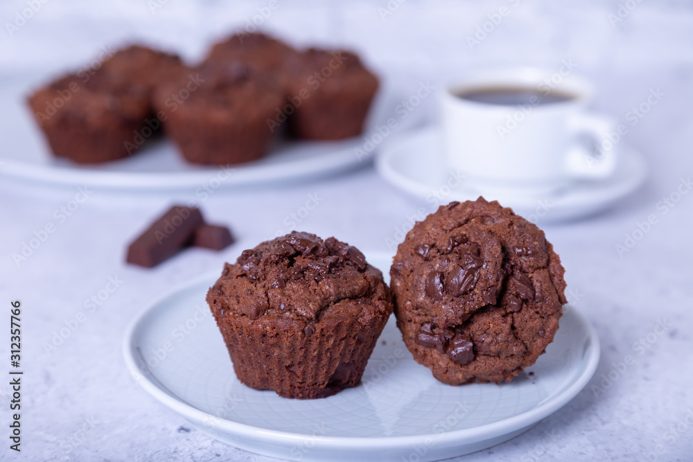 Chocolate muffins on a white plate. Homemade baking. In the background is a cup of coffee. White background. Selective focus, close up.