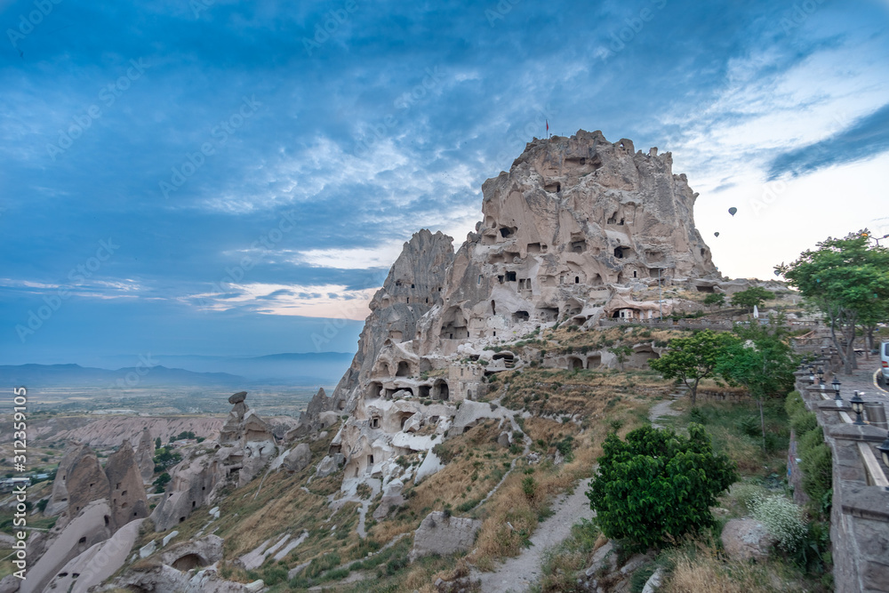 Uchisar Castle in Cappadocia, Turkey with balloons in background
