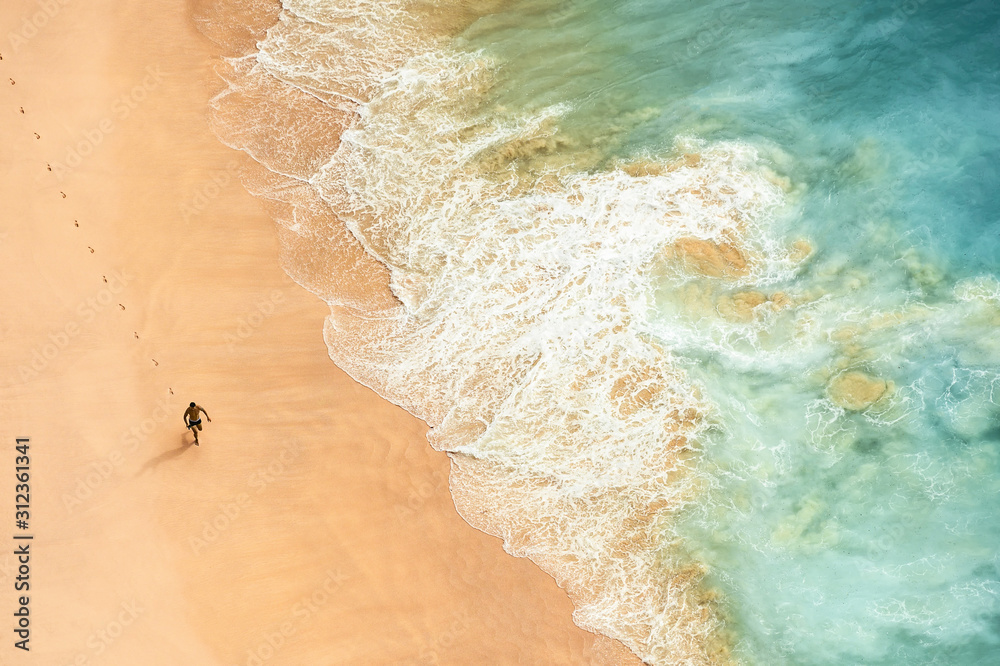 View from above, stunning aerial view of a person running on a beautiful beach bathed by a turquoise sea during sunset. Kelingking beach, Nusa Penida, Indonesia.  - obrazy, fototapety, plakaty 