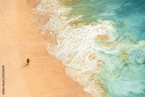 View from above, stunning aerial view of a person running on a beautiful beach bathed by a turquoise sea during sunset. Kelingking beach, Nusa Penida, Indonesia. 
