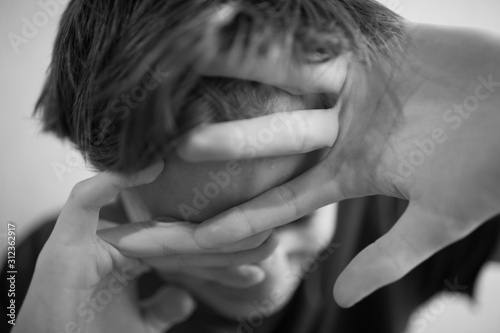 A teenager in a state of shock and depression squeezes his head with his hands on a light background