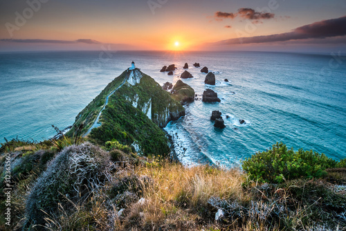 Nugget point. Rock Cliffs and Lighthouse in the South Island. Magical colorful daybreak on rock cliffs with lighthouse in Otago district close to Dunedin, South Island of New Zealand. Sun rays and bea photo