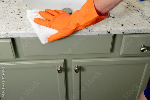 Hand Wearing an Orange Glove Cleaning a Stone Bathroom Counter