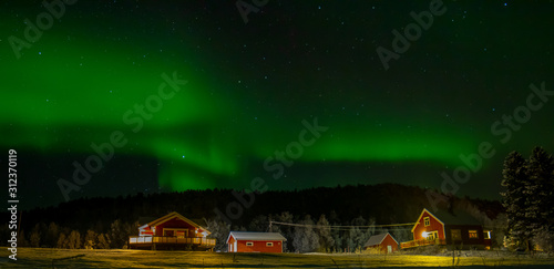 Panoramic Northern lights above wooden red cabin in Northern norway