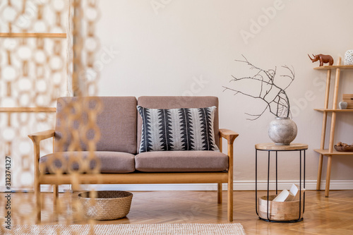 Stylish interior of living room at cozy apartment with brown wooden sofa, coffe table, bookstand , pillow, flowers and elegant accessories. Beige and japandi concept. Modern home staging. Template. photo