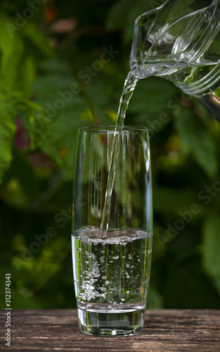 pouring Glass of clear water from jug on nature background