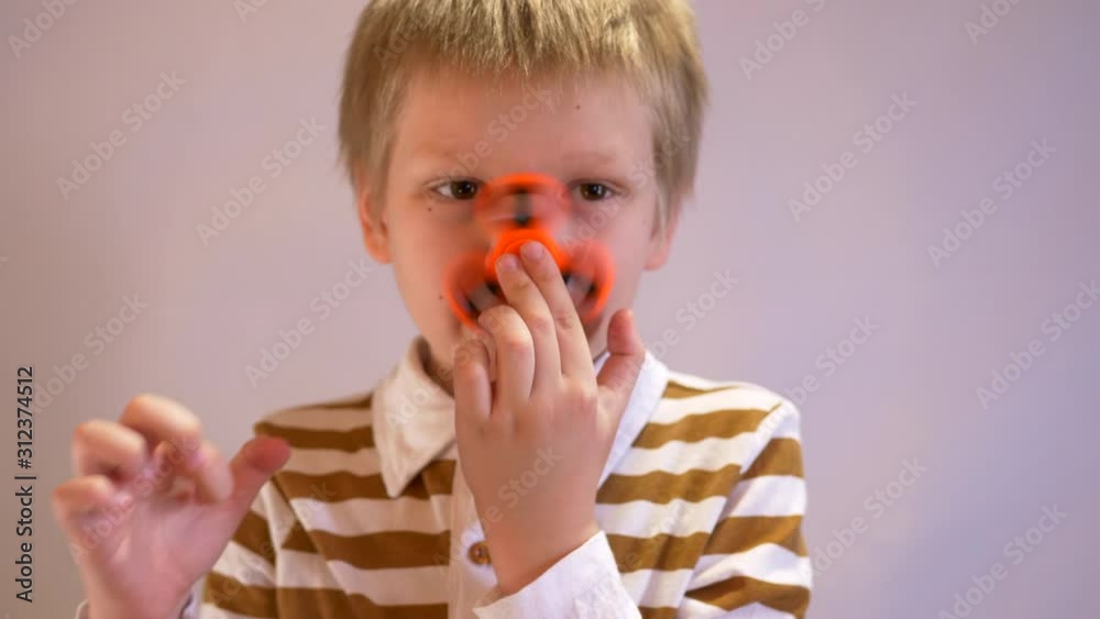Funny blond child in striped shirt twists spinner on his nose. Portrait of boy on white background. 4K. Soothing toy. Autism. Exercise for preschoolers. Falling soap bubbles Funny blond child in striped shirt twists spinner on his nose. Portrait of boy on white background. 4K. Soothing toy. Autism. Exercise for preschoolers. Falling soap bubbles