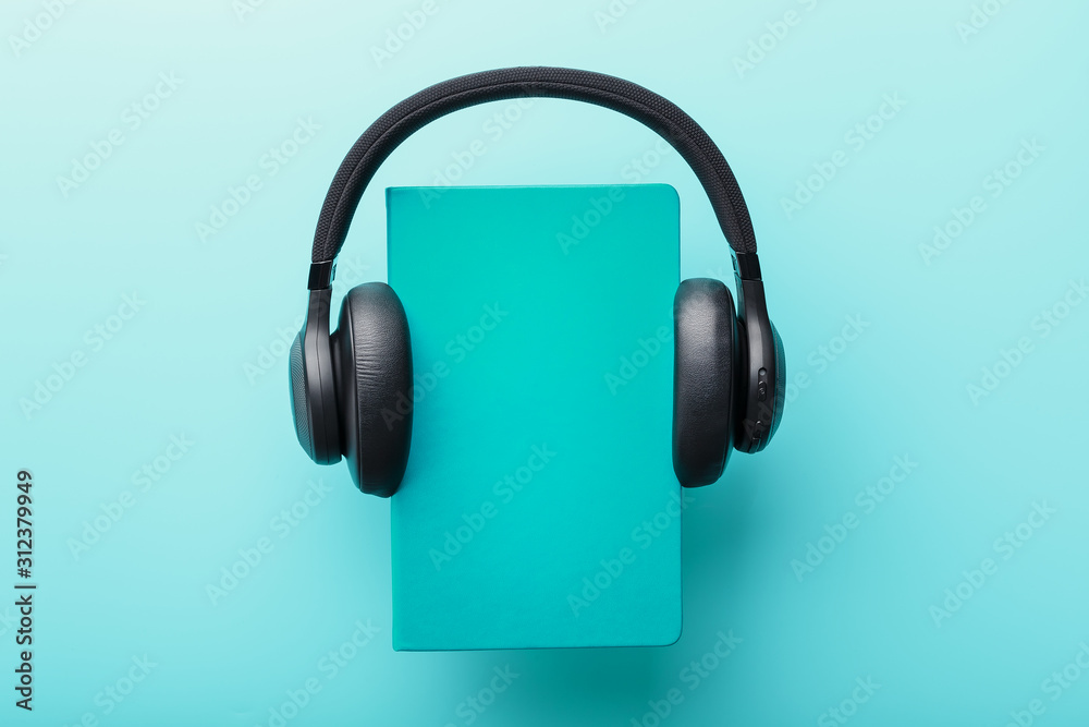 Headphones are worn on a book in a blue hardcover on a blue background, top view. Headphones are worn on a book in a blue hardcover on a blue background, top view.