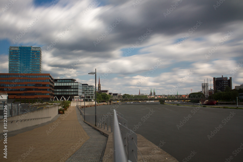 long exposure of the Überseestadt in Bremen, Germany with office buildings and cloudy sky and the river Weser in the foreground