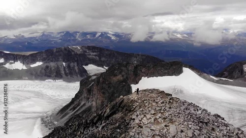 Aerial, orbit, drone shot, around mountaineers, on the Galdhopiggen mountain, tilting towards the Svellsnosbrean glacier, on a overcast day, in Jotunheimen National park photo