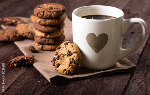 Cup of coffee with heart and chocolate chip cookies on rustic wooden background.