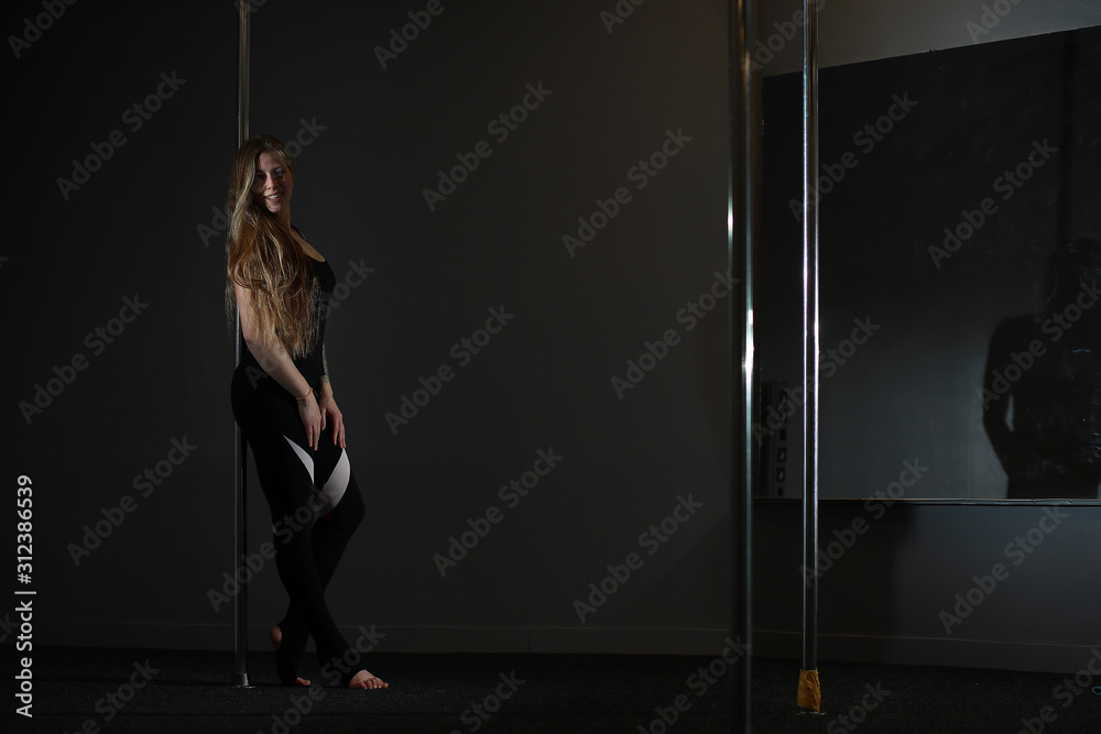 The dancer on the pylon in the studio. Girl doing exercises on a sports equipment.