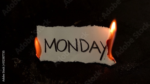 Monday word written on white paper burns. Fire with smoke and ashes on black background photo