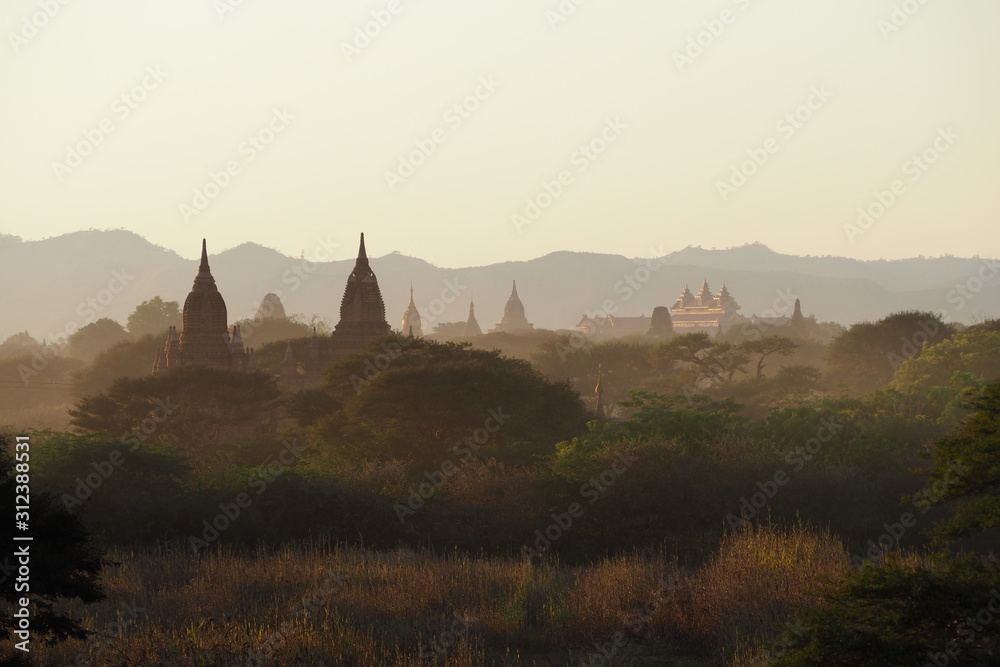 Beautiful landscape view of the old pagodas and Buddhist temples in Bagan Myanmar before sunset time with warm and clear sky and mountain background. Religious landmark for tourism destination in Asia