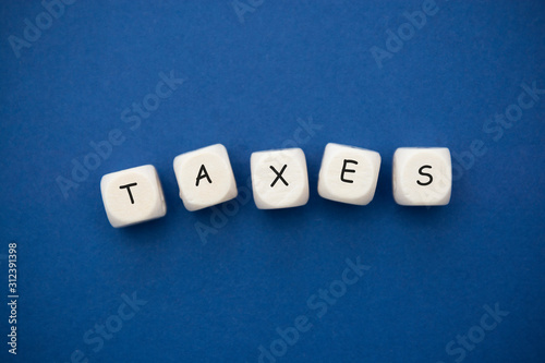 Taxes word on wooden cubes over blue bacground  top view. Finance concept.
