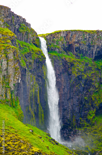 Breathtaking Grundarfoss waterfall cascade with cliff in amazing nature scenery and landscape near Grundarfjordur on Iceland in summer with green lush meadows photo