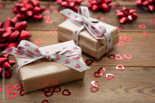 Kraft brown paper gift box with red bows and confetti, on wooden background. Valentine's Day, Birthday, Party concept.