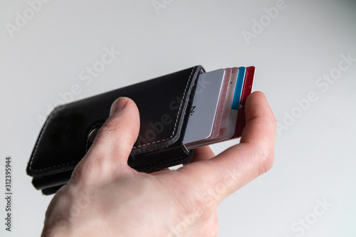 Smart minimalistic wallet, card ejector 1. Close up man's hand holding black leather wallet ejecting credit cards on isolated white background. Fashionable, slim wallet.