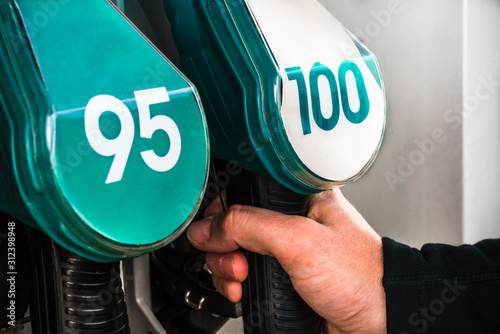 Mans hand selects 100 or 95 octane number (European RON rating) out of quality gasoline nozzle guns at petrol station refuelling stand - automotive business or environmental pollution closeup backdrop