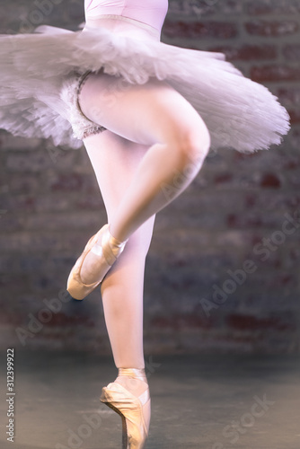 Hard work ballet technique exercise. Closeup of young attractive girls body in white balletic tulle skirt, panties and lace pointe shoes. Motion blur of elegant ballerina dancer legs.