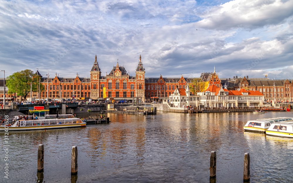 Obraz premium Panoramic view of Central Train Station in Amsterdam, architecture monument built in 1889, city's main public transportation hub. Canal with ferry boats in the foreground. Amsterdam, Netherlands.