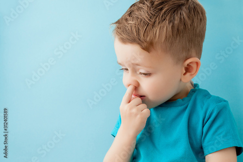 Little caucasian boy picking his nose on blue background