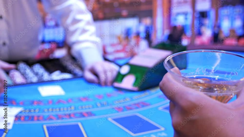 In the foreground, a poker player with a glass of champagne, in the background the dealer moves chips, tokens. Casino gambling In the foreground, a poker player with a glass of champagne, in the background the dealer moves chips, tokens. Casino gambling