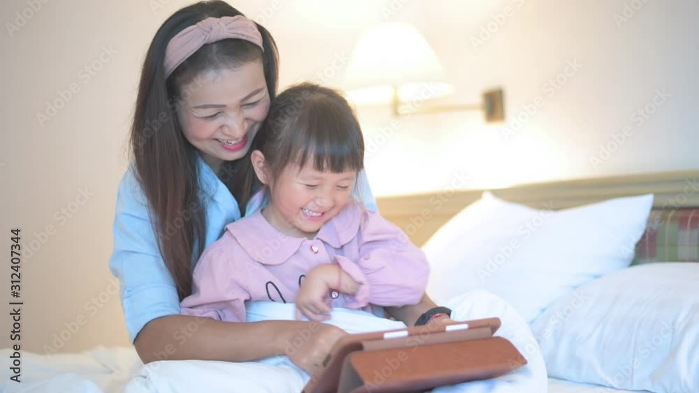 Mother and daughter using tablet with laugh happy feeling on white bed concept for happy family Mother and daughter using tablet with laugh happy feeling on white bed concept for happy family