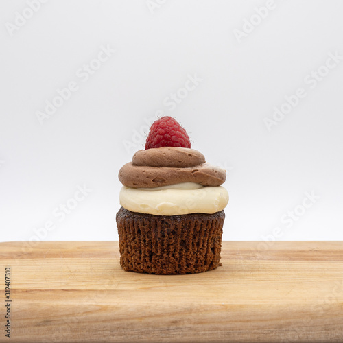 chocolate cupcake with frosting and raspberry garnish on wodden board