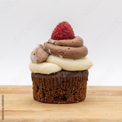 chocolate cupcake with frosting and raspberry garnish on wodden board