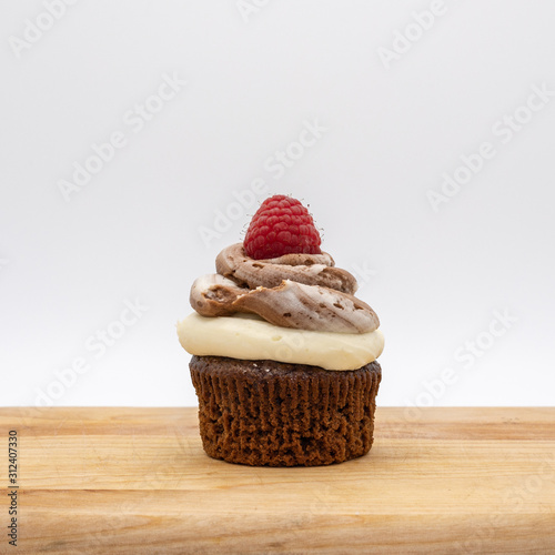 chocolate cupcake with frosting and raspberry garnish on wodden board