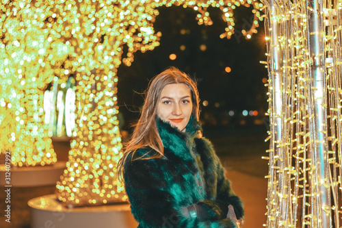 Young pretty girl in green fur coat outdoor on the glowing background