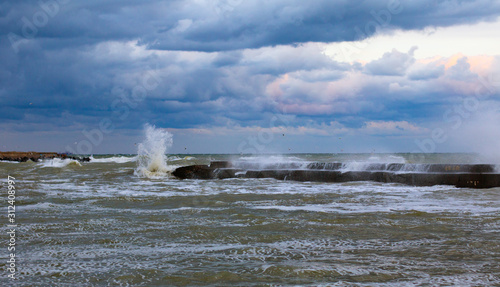 blue stormy clouds, storm at sea, waves are breaking of the pier, dirty orange water