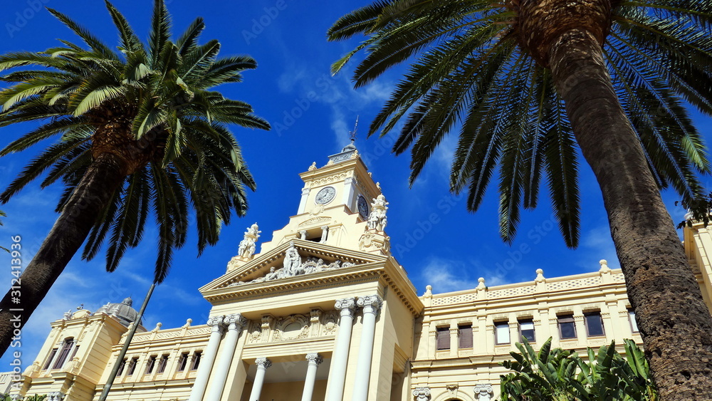 dekoratives Rathaus von Malaga fotografiert zwischen 2 großen Palmen vor blauem Himmel