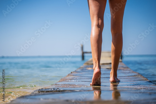 Legs of a girl walking on a wooden bridge in the middle of the ocean