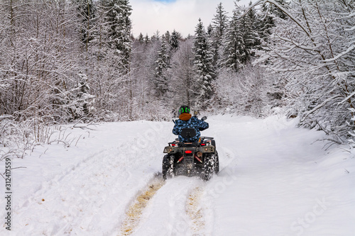 Winter landscape - view of the snowy road with a quad bike in the winter mountain forest after snowfall