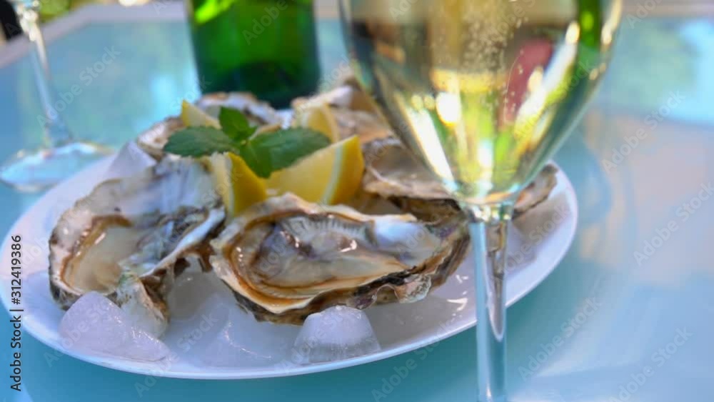 Open oysters on a white plate with ice and lemon. Panorama from a glass with champagne to plate with oysters