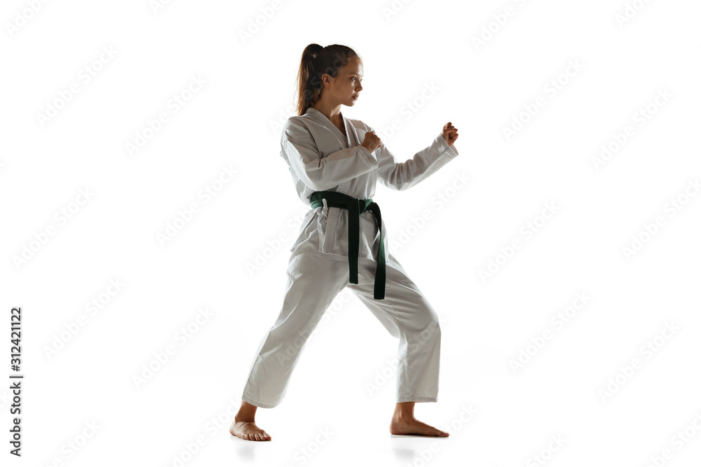 Confident junior in kimono practicing hand-to-hand combat, martial arts. Young female mongol fighter with green belt training on white studio background. Concept of healthy lifestyle, sport, action.