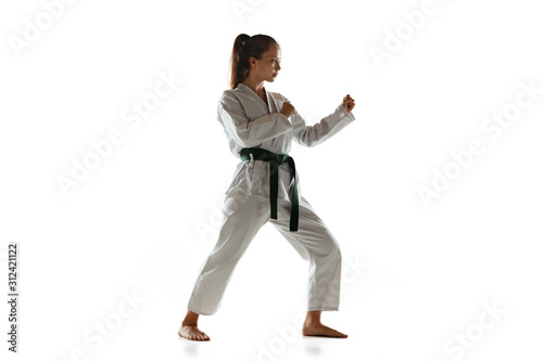Confident junior in kimono practicing hand-to-hand combat, martial arts. Young female mongol fighter with green belt training on white studio background. Concept of healthy lifestyle, sport, action. © master1305