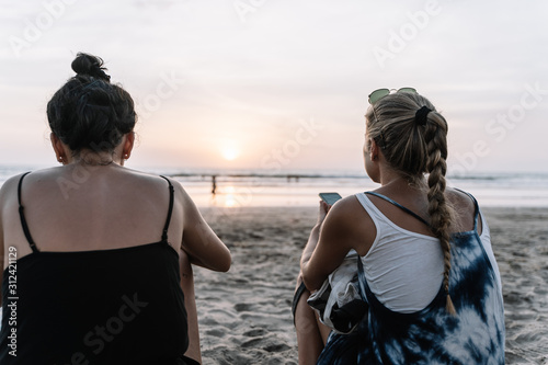 Two girls sitting on the beach watching the mobile