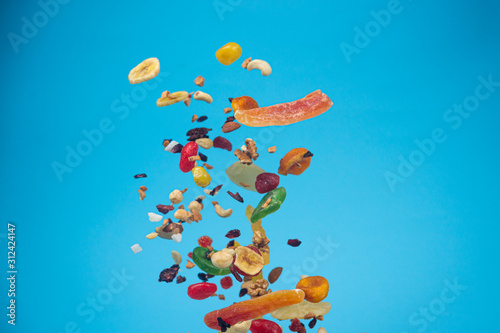 Dried and candied fruits and nuts flying on blue background. Stock photo of healty and nutrient food.