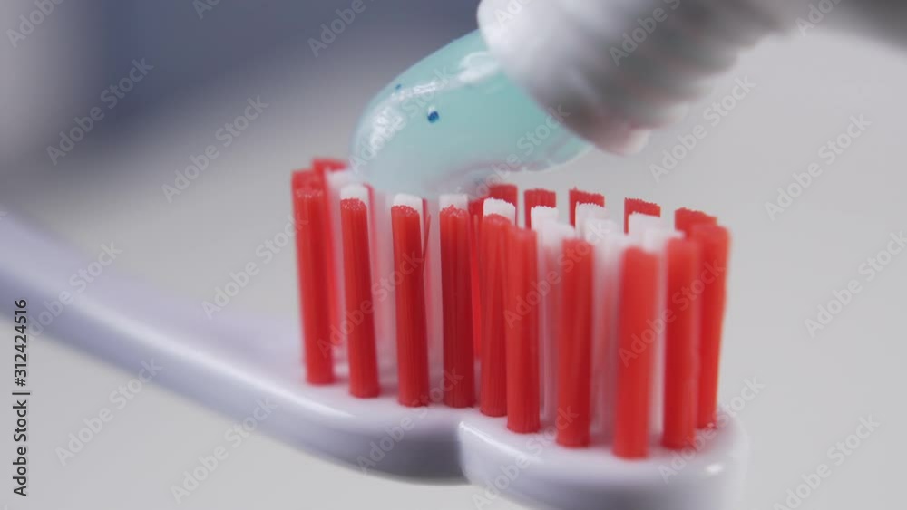 Squeezing blue toothpaste onto the red bristles of a plastic toothbrush in the bathroom closeup. Personal hygiene products Squeezing blue toothpaste onto the red bristles of a plastic toothbrush in the bathroom closeup. Personal hygiene products