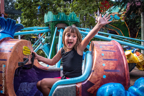 Eye-level, Laughing waving girl on a ride at amusement park, smiling, excited