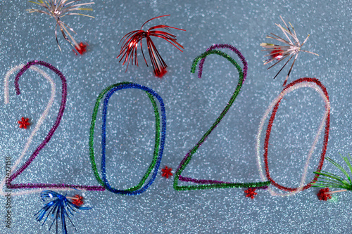 Party postcard with sparkling colorful numbers made by pipe cleaners or whistle washer, sparkling turquoise background with red festive stars. High angle view. Concept for party 2020 and New Year.